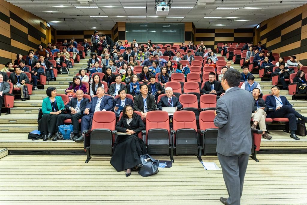 Professional setting of a business conference with attendees and a presenter in an auditorium.