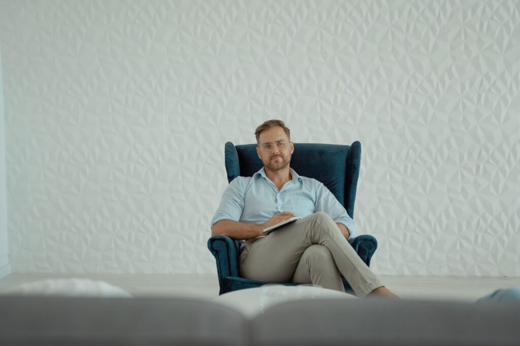 A thoughtful man sitting cross-legged in an armchair against a stylish white background.